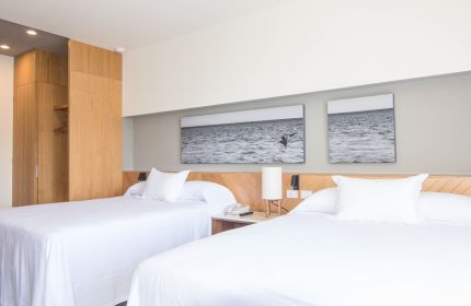 Hotel Mio Vallarta Adults Only room. Gay-friendly hotel featuring two beds with white linens and ocean-themed art. Modern, clean design.