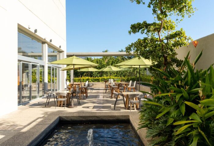 Hotel Mio Vallarta Adults Only gay-friendly hotel outdoor dining area with umbrellas, tables, chairs, water feature, and lush greenery.