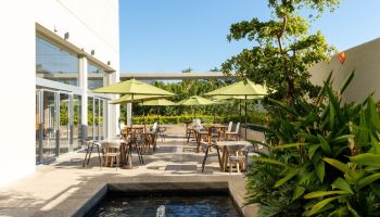 Hotel Mio Vallarta Adults Only gay-friendly hotel outdoor dining area with umbrellas, tables, chairs, water feature, and lush greenery.