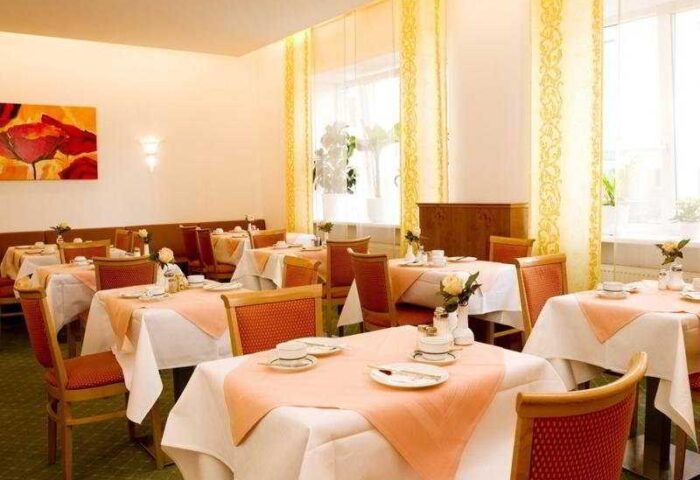 Hotel Müller Munich's dining room. Tables with white tablecloths and orange accents. Gay-friendly hotel in Munich, Germany.