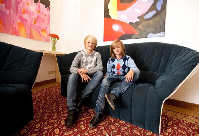 Hotel Müller Munich: Two young boys sit on a blue sofa in the gay-friendly Hotel Müller. Colorful art adorns the walls. Munich travel.