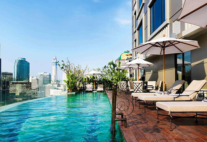 Rooftop infinity pool at gay-friendly Hotel Muse Bangkok Langsuan MGallery Collection. City view, sun loungers, umbrellas. Luxury travel.