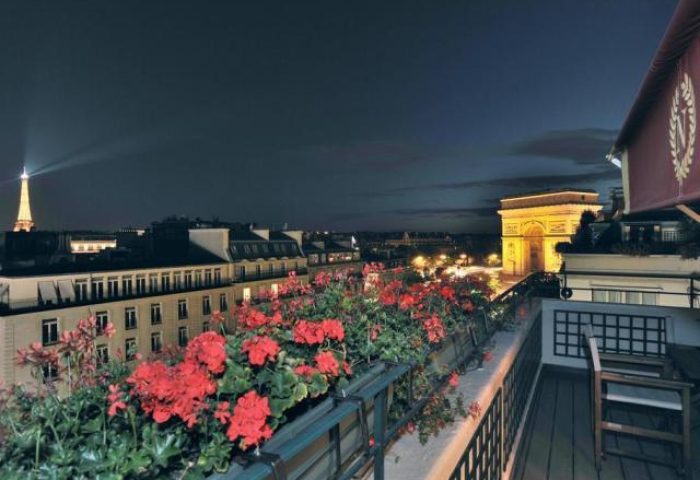 Hotel Napoleon gay-friendly hotel pet-friendly view: Eiffel Tower and Arc de Triomphe from a balcony with red flowers at night in Paris.