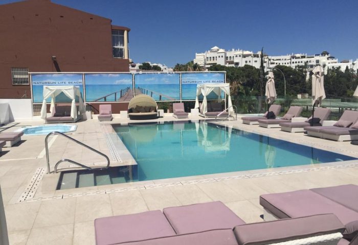 Hotel Natursun pool. Gay-friendly hotel with sunbeds and clear blue water. Natursun Life Beach banner in the background.