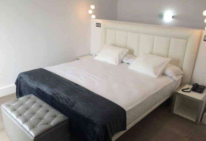 Hotel Natursun's gay-friendly room: a comfortable bed with white linens, a gray throw, and a stylish ottoman. Perfect for gay travelers.