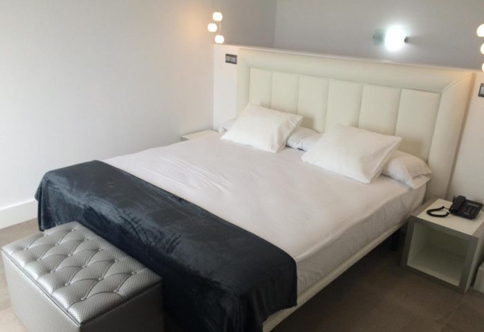 Hotel Natursun's gay-friendly room: a comfortable bed with white linens, a gray throw, and a stylish ottoman. Perfect for gay travelers.