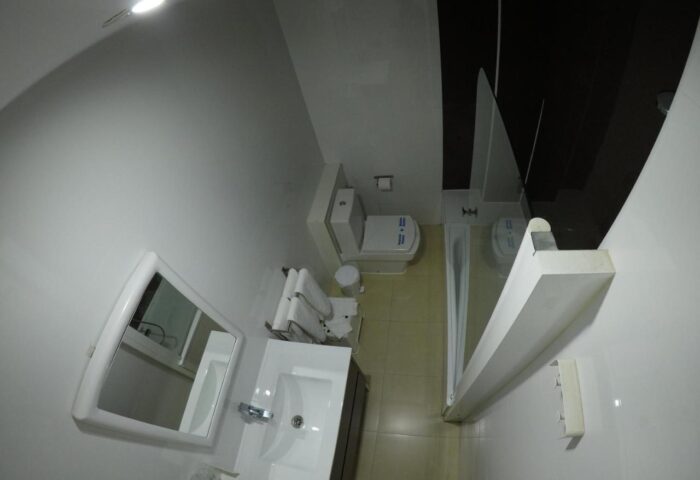 Hotel Natursun gay-friendly bathroom. View of the toilet, sink, mirror, and shower. Hotel for gay men's travel in Gran Canaria.