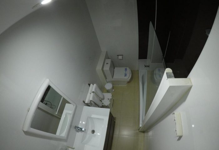 Hotel Natursun gay-friendly bathroom. View of the toilet, sink, mirror, and shower. Hotel for gay men's travel in Gran Canaria.