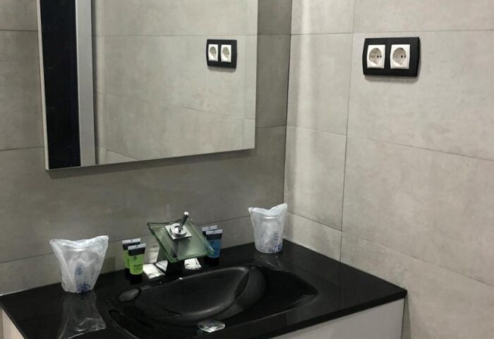 Hotel Natursun's gay-friendly bathroom. Modern sink with black countertop, white drawers, large mirror, and toiletries. Hotel room interior.