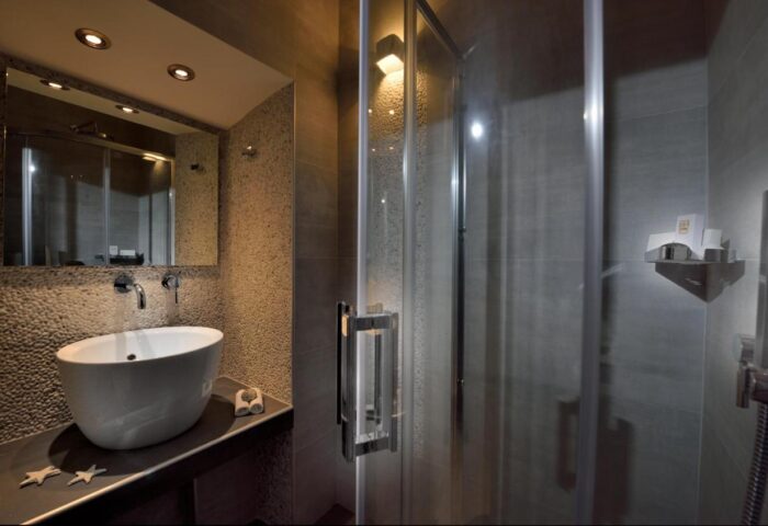 Hotel Nazos Mykonos Town bathroom. Modern sink, shower, and pebble-textured wall. Gay-friendly hotel in Mykonos.