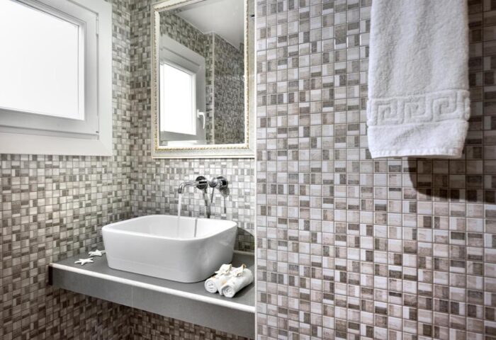Hotel Nazos Mykonos Town bathroom. Gay-friendly hotel with modern sink, mosaic tiles, mirror, and towel. Stylish design in Mykonos Town.