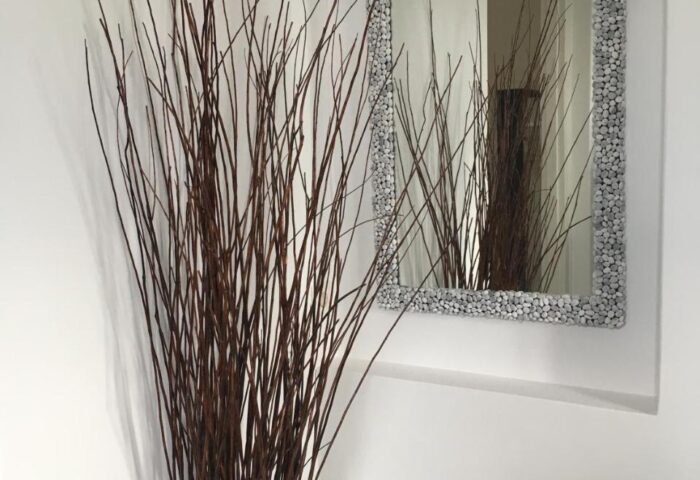 Hotel Nazos, Mykonos Town detail. Vase of branches beside a mirror with a pebble frame. Gay-friendly hotel interior design.