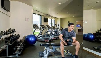 Hotel Nikko Saigon's gym: A gay-friendly hotel. Man lifting weights on a bench. Treadmills, dumbbells, and exercise ball are also visible.