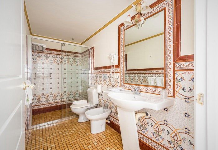 Hotel Noucentista gay-friendly bathroom featuring a shower, toilet, bidet, and sink with decorative tilework. Ideal for gay travel.