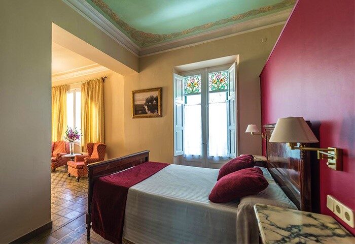 Hotel Noucentista's gay-friendly room: a bedroom with a double bed, a sitting area, and a window with colored glass. Gay travel.