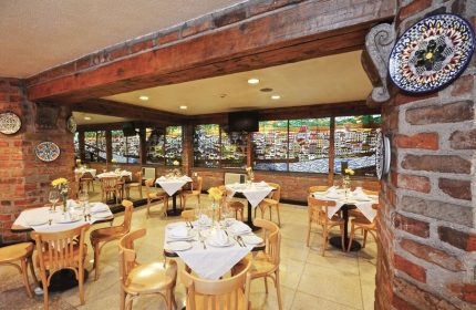 Hotel PF gay-friendly restaurant interior. Tables set with white linens, wood chairs, brick walls, and decorative plates. Cityscape view.