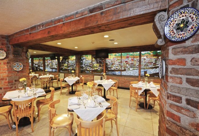 Hotel PF gay-friendly restaurant interior. Tables set with white linens, wood chairs, brick walls, and decorative plates. Cityscape view.