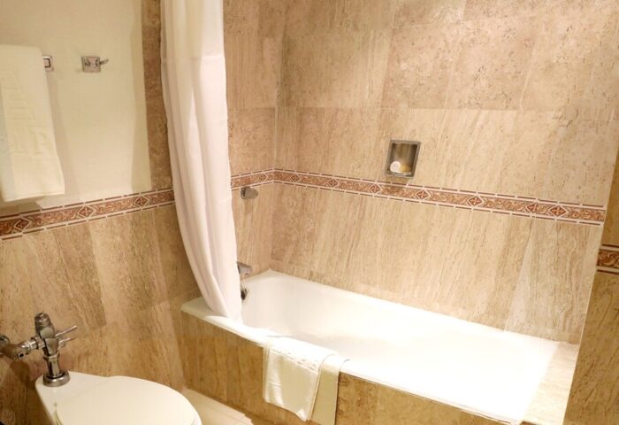 Bathroom at Gay-Friendly Hotel PF. Bathtub with shower curtain, toilet, and beige tile. Gay travel accommodations for discerning men.