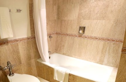Bathroom at Gay-Friendly Hotel PF. Bathtub with shower curtain, toilet, and beige tile. Gay travel accommodations for discerning men.