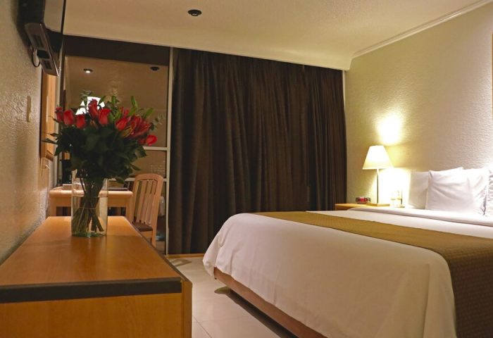 Hotel PF room interior. Gay-friendly Hotel PF features a bed, roses, desk, and curtains. Ideal for gay men's travel, offering comfort and style.