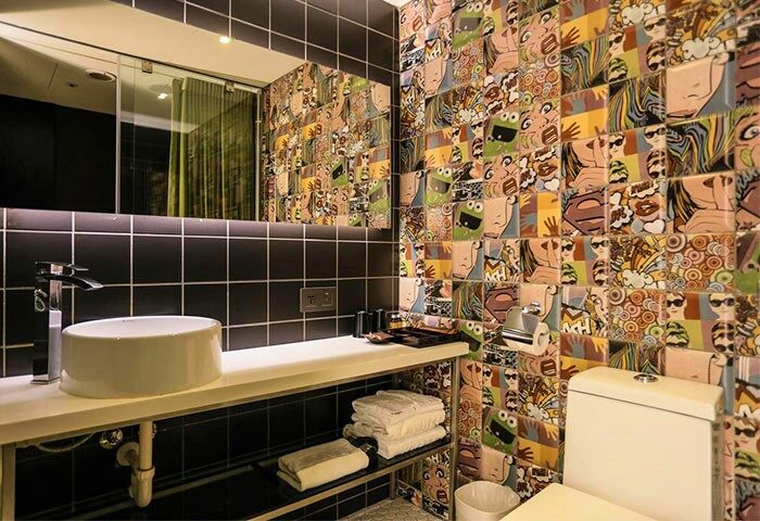 Hotel PaPa Whale's bathroom. Gay-friendly hotel bathroom with pop art tiles, black tile accents, modern sink, and shelf with towels.
