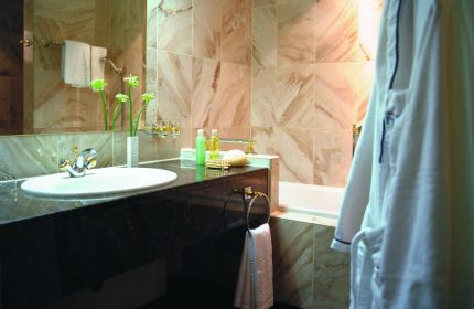 Hotel Palace Berlin bathroom, pet-friendly. Sink, marble tiles, and a bathrobe. Gay-friendly hotel with luxury amenities.
