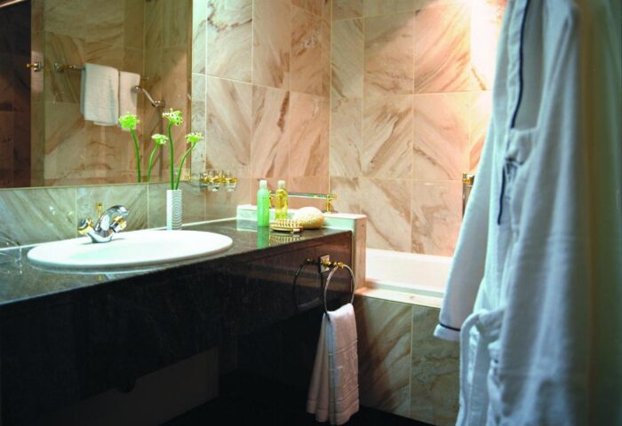 Hotel Palace Berlin bathroom, pet-friendly. Sink, marble tiles, and a bathrobe. Gay-friendly hotel with luxury amenities.