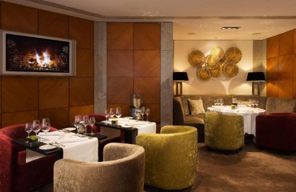 Hotel Palace Berlin gay-friendly dining: Tables set with wine glasses, plush chairs, and a fireplace on TV. Pet-friendly luxury.