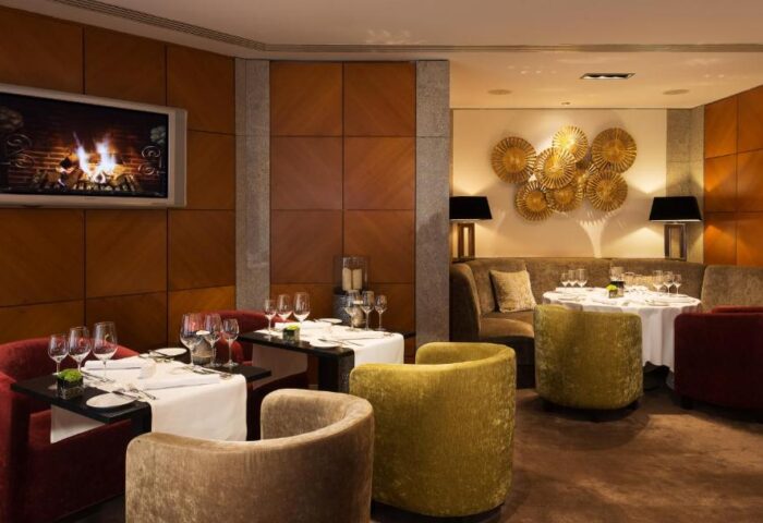 Hotel Palace Berlin gay-friendly dining: Tables set with wine glasses, plush chairs, and a fireplace on TV. Pet-friendly luxury.