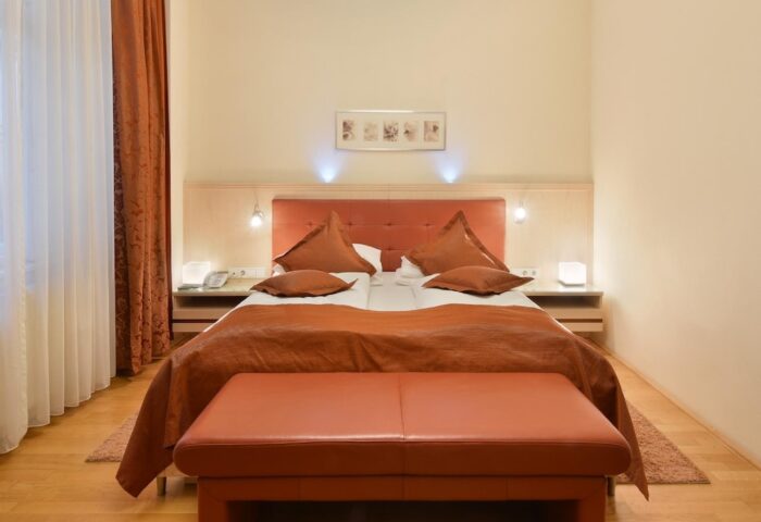 Hotel Pensione Wildner gay-friendly room. Double bed with orange pillows and blanket. Bench at the foot. Gay men travel advice.