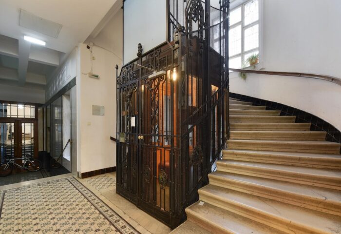 Interior of Hotel Pensione Wildner, a gay-friendly hotel. Features a vintage elevator with ornate metalwork and a marble staircase.