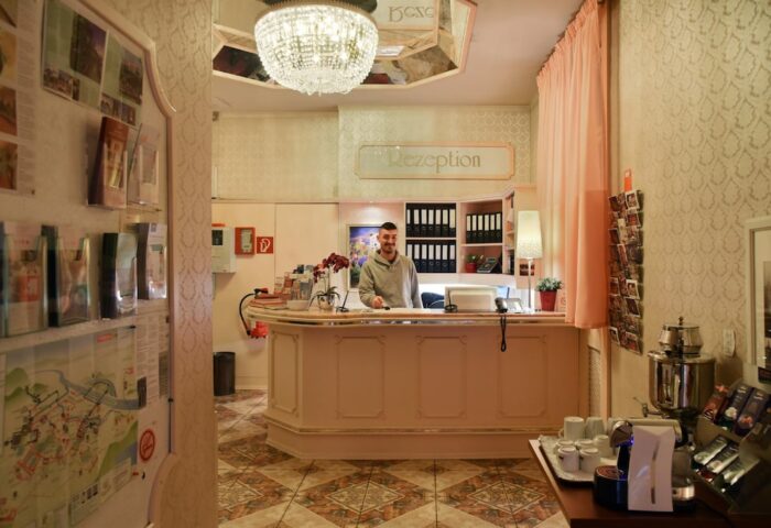 Hotel Pensione Wildner's reception area. A man stands behind the counter. Gay-friendly hotel with a chandelier and coffee station.