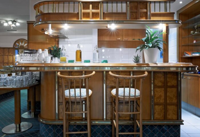 Hotel Pensione Wildner's bar area. Gay-friendly hotel interior with wooden bar, stools, and breakfast setup. A welcoming space for gay travelers.