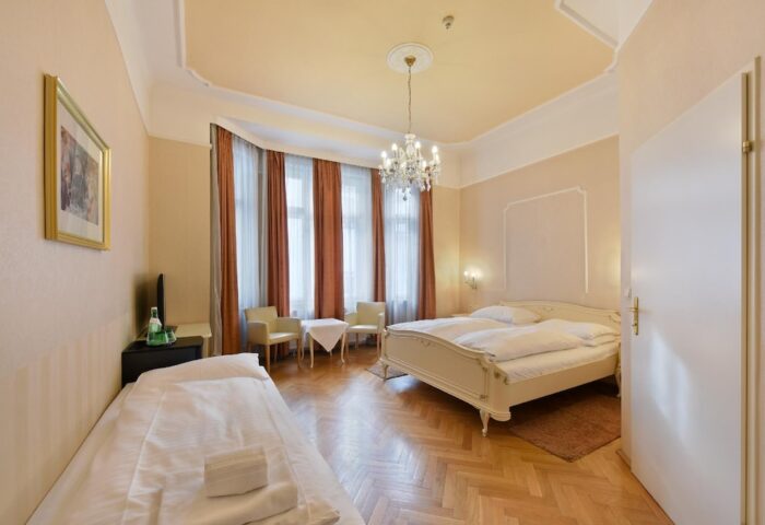 Gay-Friendly Hotel Pensione Wildner bedroom. Room with double bed, single bed, chandelier, curtains, and chairs. Gay travel advice.
