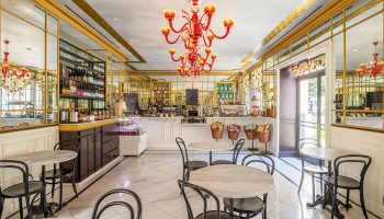 Interior of Hotel Per La, Autograph Collection, a gay-friendly hotel. Cafe with marble tables, black chairs, and a red chandelier.