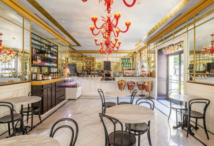 Interior of Hotel Per La, Autograph Collection, a gay-friendly hotel. Cafe with marble tables, black chairs, and a red chandelier.