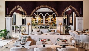 Hotel Per La, Autograph Collection interior. Gay-friendly hotel bar area with white sofas, marble tables, arched doorways, and a well-stocked bar.