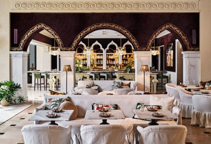 Hotel Per La, Autograph Collection interior. Gay-friendly hotel bar area with white sofas, marble tables, arched doorways, and a well-stocked bar.