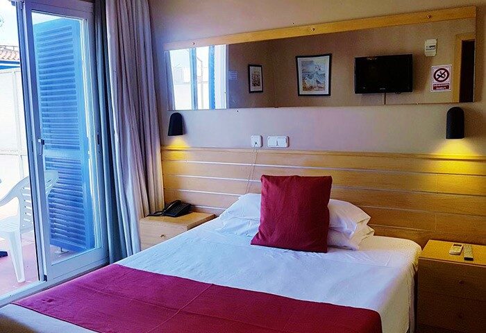 Hotel Piccadilly Sitges gay-friendly room. Balcony view, double bed with red accents, TV, and modern decor. A relaxing stay in Sitges.