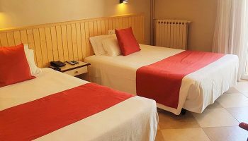 Hotel Piccadilly Sitges gay-friendly room. Two beds with red accents, bedside table, and tiled floor. A comfortable stay for gay travelers.