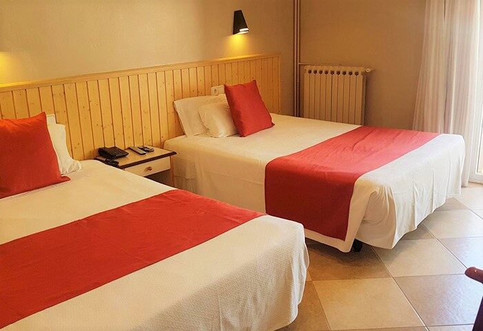 Hotel Piccadilly Sitges gay-friendly room. Two beds with red accents, bedside table, and tiled floor. A comfortable stay for gay travelers.