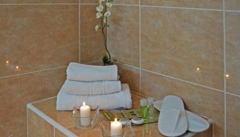 Hotel Piccadilly Sitges gay-friendly hotel bathroom detail. Stacked towels, candles, orchid, slippers, and toiletries. Relaxing spa vibe.