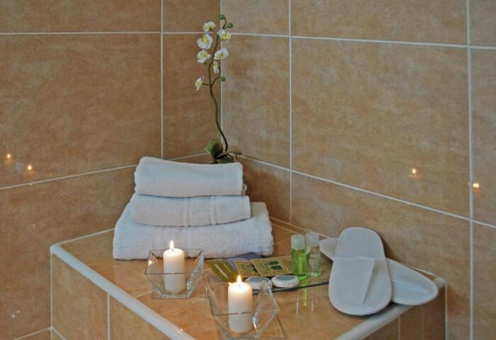 Hotel Piccadilly Sitges gay-friendly hotel bathroom detail. Stacked towels, candles, orchid, slippers, and toiletries. Relaxing spa vibe.