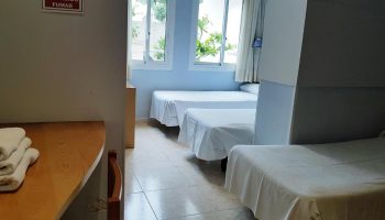 Hotel Piccadilly Sitges gay-friendly room. Interior view of a room with three beds, white linens, and light blue walls. Gay travel in Sitges.