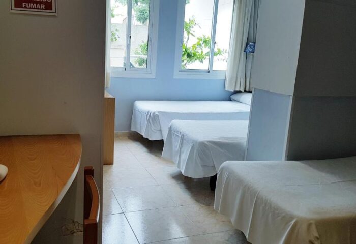 Hotel Piccadilly Sitges gay-friendly room. Interior view of a room with three beds, white linens, and light blue walls. Gay travel in Sitges.