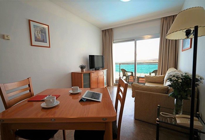 Gay-Friendly Hotel Port Sitges room with sea view. Hotel room interior with table, chairs, sofa, and balcony overlooking the sea.