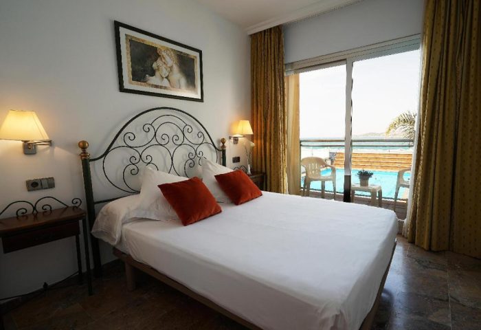 Hotel Port Sitges gay-friendly room with pool view. Bedroom interior with double bed, balcony, and modern decor. Ideal gay travel choice.