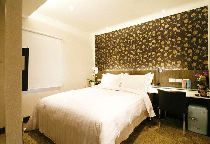 Hotel Puri Ximen bedroom. Gay-friendly hotel room with double bed, desk, floral wallpaper, and mini-fridge. Comfy stay in Taipei.