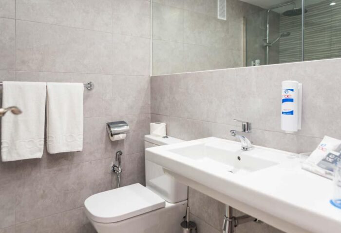 Bathroom at AluaSun Flamingo, a gay-friendly hotel. Features a toilet, sink, mirror, towels, and toiletries. Ideal for gay travel.