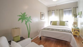 Hotel Royal gay-friendly room. Bedroom with palm tree wall art, white bedding, and chair. Comfortable gay travel lodging.